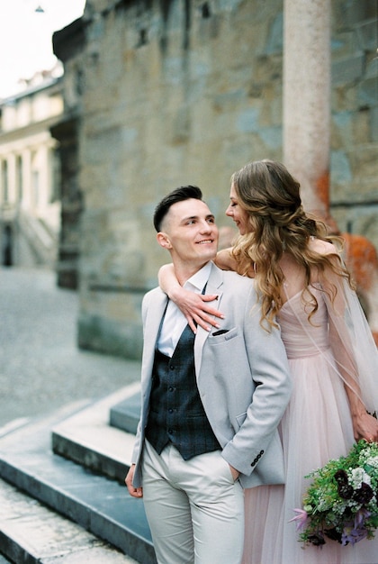 Smiling bride hugs groom from behind on the steps bergamo italy