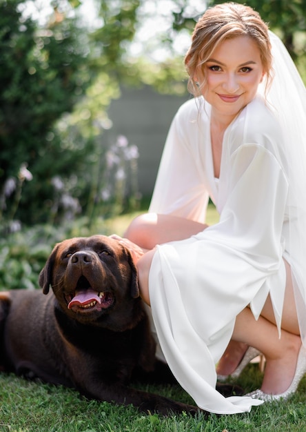 Photo smiling bride in robe touching dog sitting in park