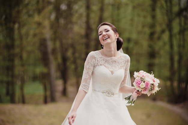 ピンクの花束と白いドレスを着た笑顔の花嫁。春の結婚式