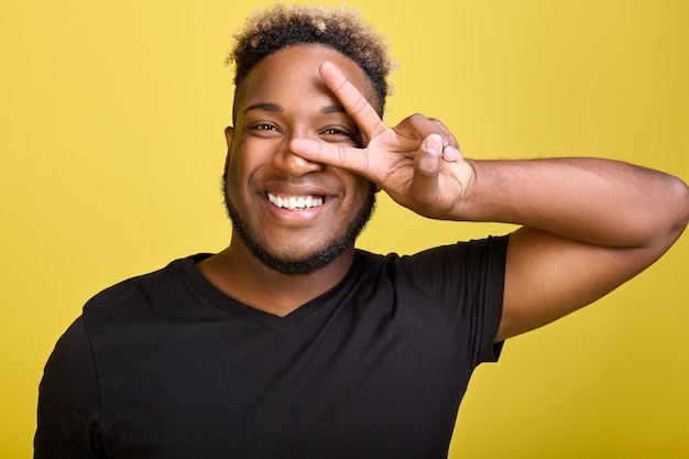 Smiling broadly africanamerican demonstrates peace and kindness around him the symbol of peace shows with his right hand a darkskinned guy in modern everyday clothes on a yellow background
