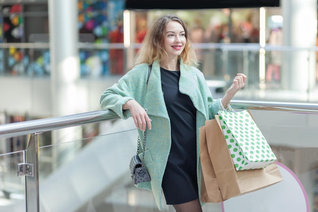 Smiling broadly cute caucasian woman with braces and curly hair holding shopping bags in the mall