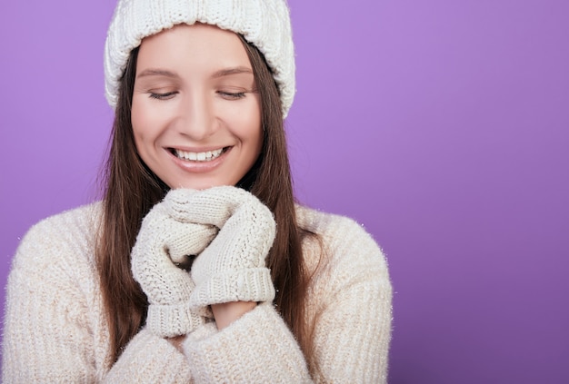 ニット帽とミトンで笑顔の茶色の髪の女性は、あごの下で手を握りしめました。