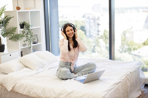 Smiling brunette female in wireless headphones enjoying favorite song