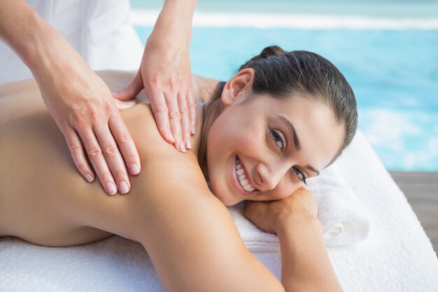 Smiling brunette getting a massage poolside looking at camera outside at the spa