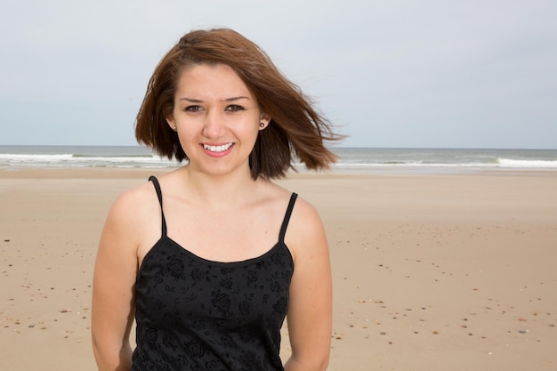 Foto sorridente ragazza bruna in abito nero in posa sulla spiaggia