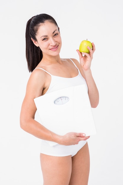 Smiling brunette holding weighing scales and apple