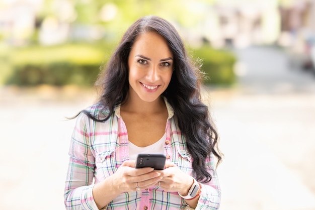 A smiling brunette is writing messages on her mobile phone