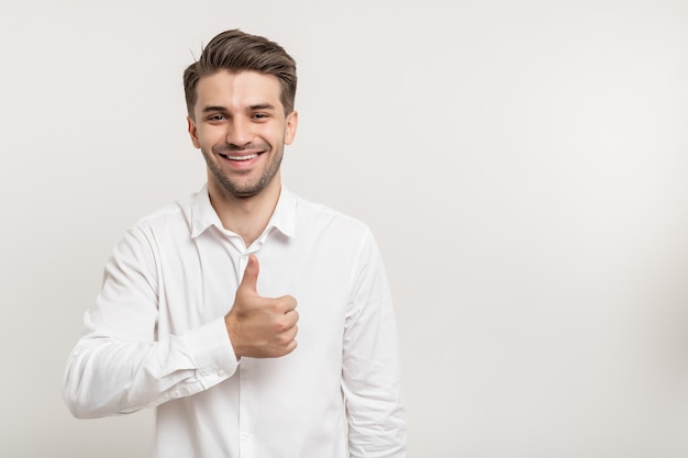 smiling brunette man in white shirt smiling showing thumb up at camera isolated on white background