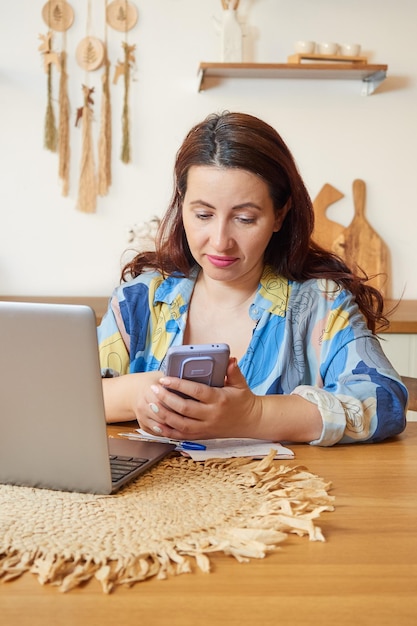 Smiling brunette uses a mobile phone works on a laptop The concept of remote work learning