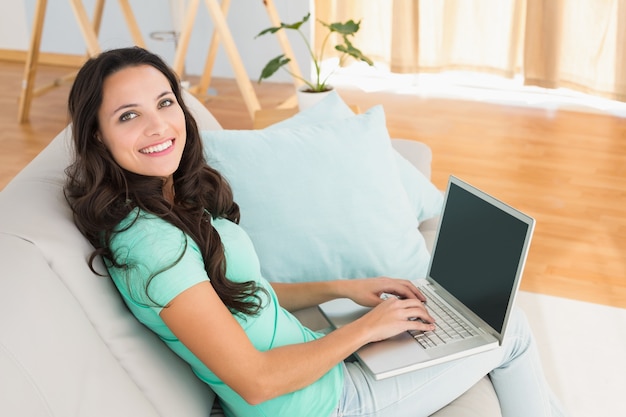 Smiling brunette using her laptop on sofa