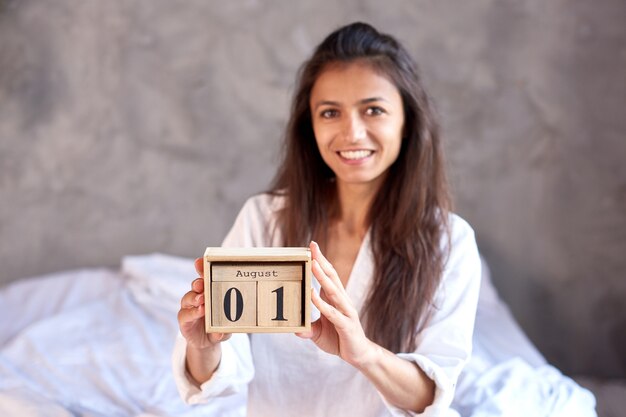 smiling brunette woman hold wooden perpetual calendar with august 1 date last month of summer