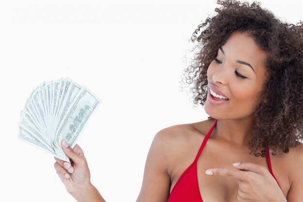 Smiling brunette woman pointing a fan of dollar notes