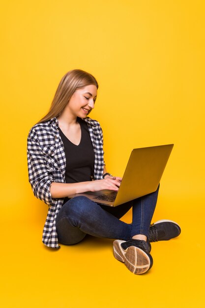 Smiling brunette woman in sweater sitting on the floor with laptop computer