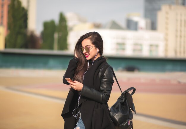 smiling brunette woman tourist in glasses listen music on cell telephone, standing at the street