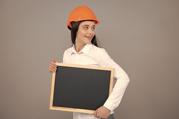 Smiling business builder woman with board portrait on gray Woman worker builder hold sign board blank Building hardhat helmet