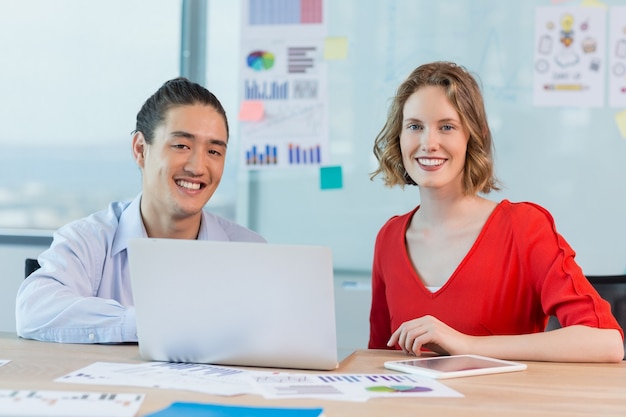 Smiling business colleagues discussing over laptop in conference room