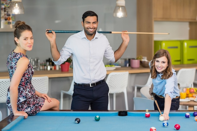 Smiling business colleagues playing pool in office space