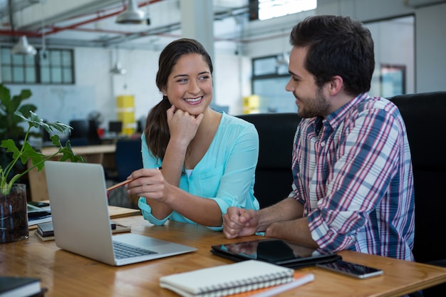 Smiling business executives discussing over laptop