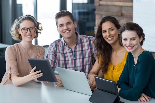 Smiling business executives sitting in office with digital tablet and laptop on table