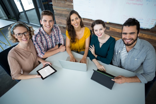 Smiling business executives sitting in office with digital tablet and laptop on table