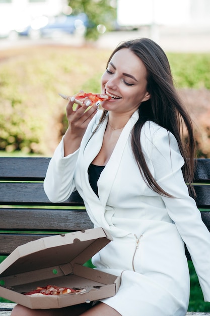 Smiling business girl eating pizza at street