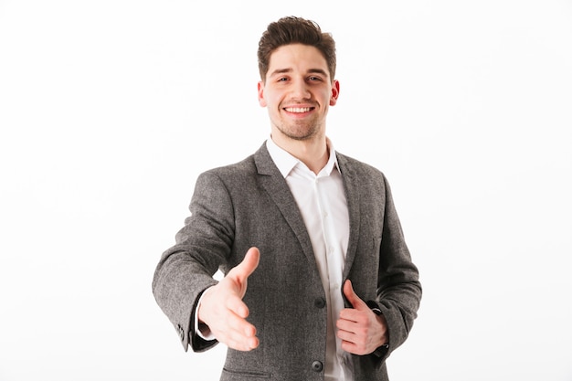 Smiling business man in jacket giving his hand to handshake  over white wall