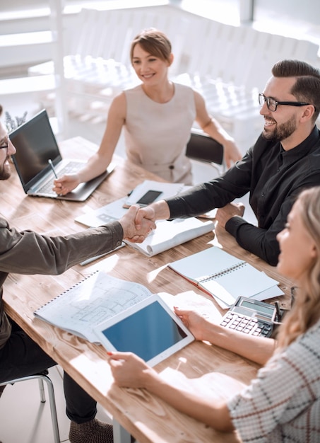 Foto partner commerciali sorridenti che stringono la mano a una riunione di lavoro