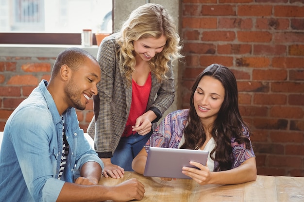 Smiling business people discussing over tablet in creative office