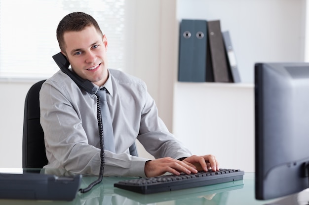 Smiling business on the phone and writing on his computer