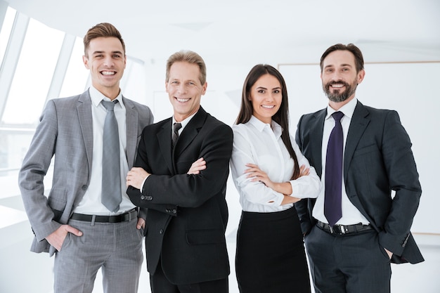 Sorridente team aziendale in piedi in ufficio e guarda la telecamera