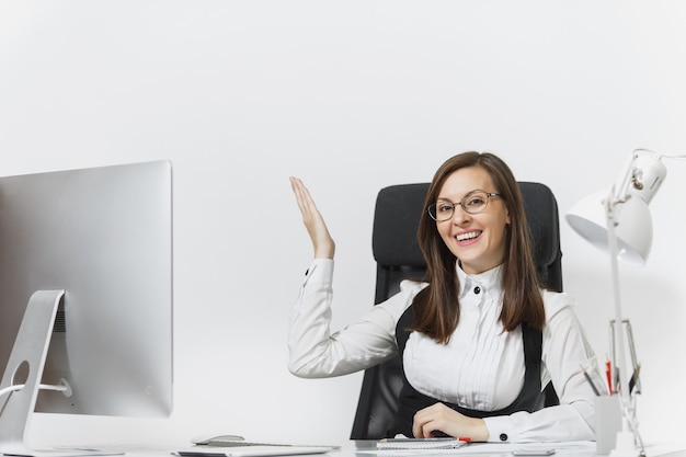 Smiling business woman sitting at the desk, working at computer with documents in light office