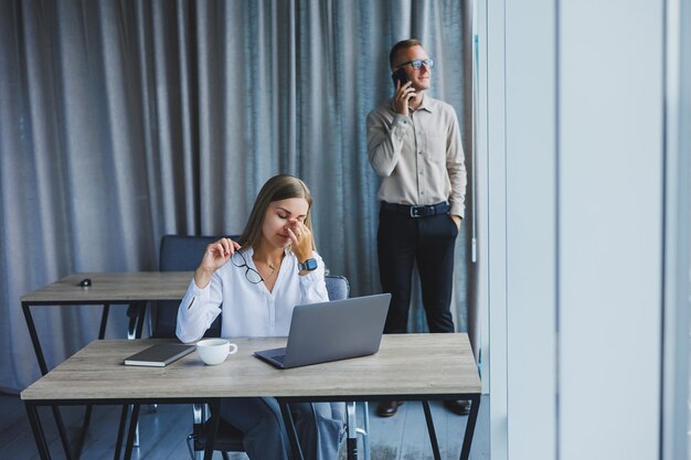 Sorridente donna d'affari seduta a un tavolo con un computer portatile tenendo la schiena al suo partner seduto al desktop il concetto di lavoro di squadra di successo