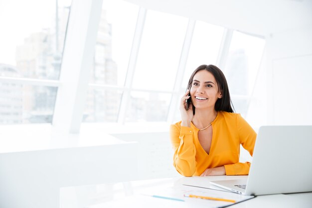 Smiling Business woman talking at phone and sitting by the table in office