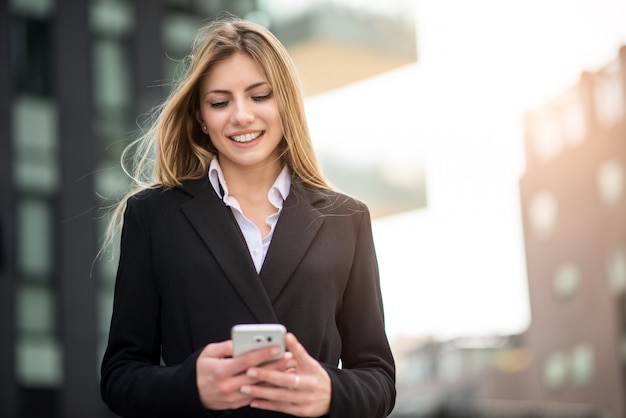 Donna sorridente di affari che per mezzo del suo telefono cellulare