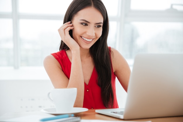 Donna d'affari sorridente che usa il portatile vicino al tavolo in ufficio