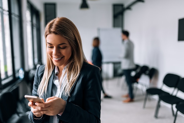 Donna sorridente di affari che utilizza telefono durante una pausa. colleghi in piedi sullo sfondo