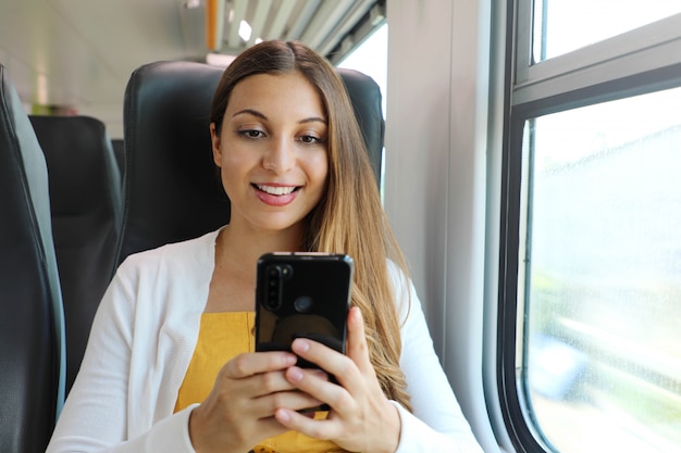 Sorridente donna d'affari utilizzando smartphone social media app mentre si reca al lavoro in treno.