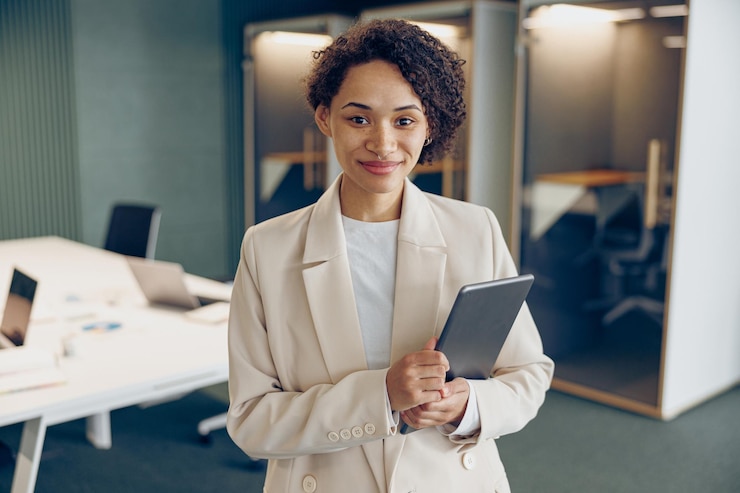Photo smiling business woman with digital tablet standing on modern office background and looks camera