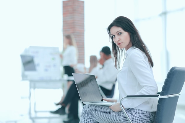 Улыбаясь бизнес-леди с ноутбуком на офисном размытом фоне.
