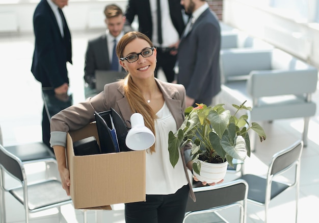 Улыбающаяся деловая женщина с личными вещами стоит в современном офисе в первый рабочий день