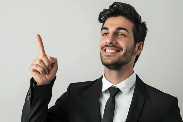 Smiling businessman in black suit pointing up on white background