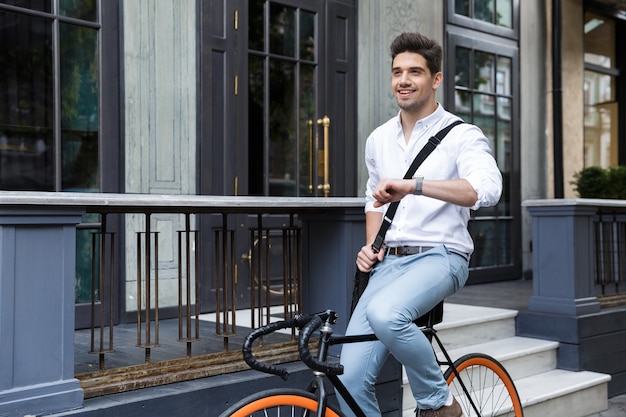 Smiling businessman dressed in shirt riding on a bicycle