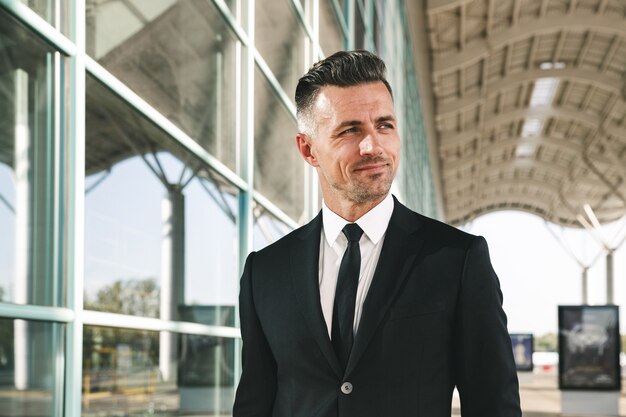 Smiling businessman dressed in suit walking outside airport