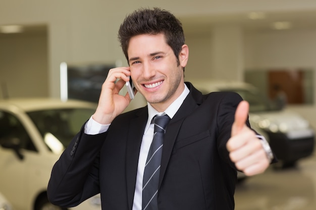 Smiling businessman giving thumbs up on phone