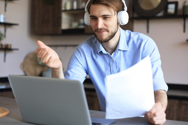 Smiling businessman greeting colleagues in video conference and negotiating distantly from home.