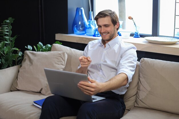 Smiling businessman greeting colleagues in video conference and negotiating distantly from home.