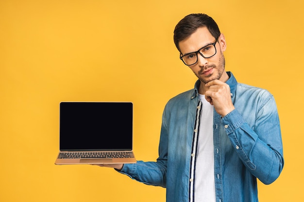 Фото Улыбающийся бизнесмен держит пустой экран ноутбука, изолированный на желтом фоне, смотрит в камеру