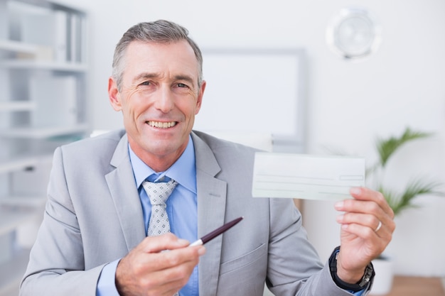 Smiling businessman holding cheque in his office 