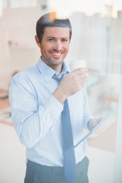 窓の外を見て錠剤と使い捨てカップを保持している笑顔のビジネスマン