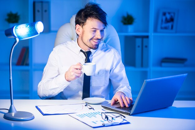 Улыбающийся бизнесмен работает на ноутбуке в офисе.